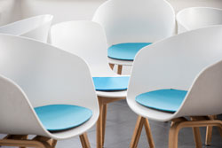 Das Foto zeigt mehrere weiße Stühle mit hellblauen Sitzauflagen, die quer aneinander stehen.